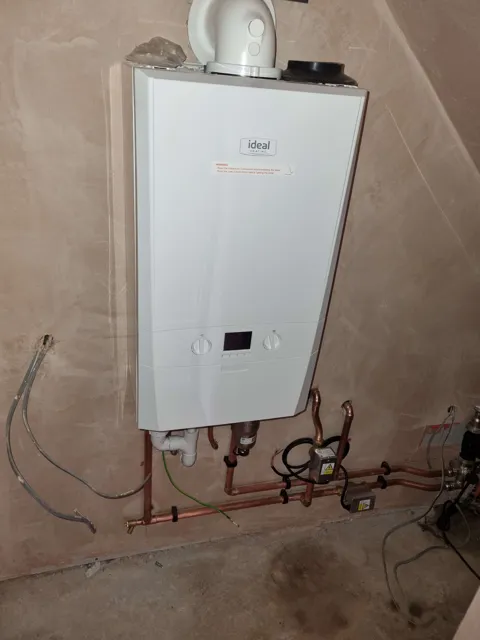 Wall-mounted boiler and pipework in an unfinished interior.