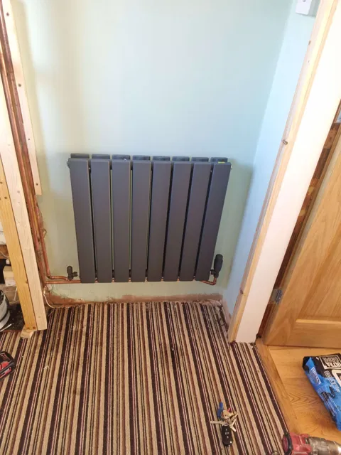 Vertical radiator and exposed floor pipework during renovation.