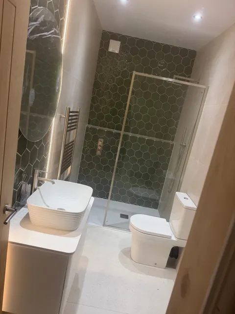 Bathroom with green hexagonal shower tiles, glass enclosure, basin and toilet.