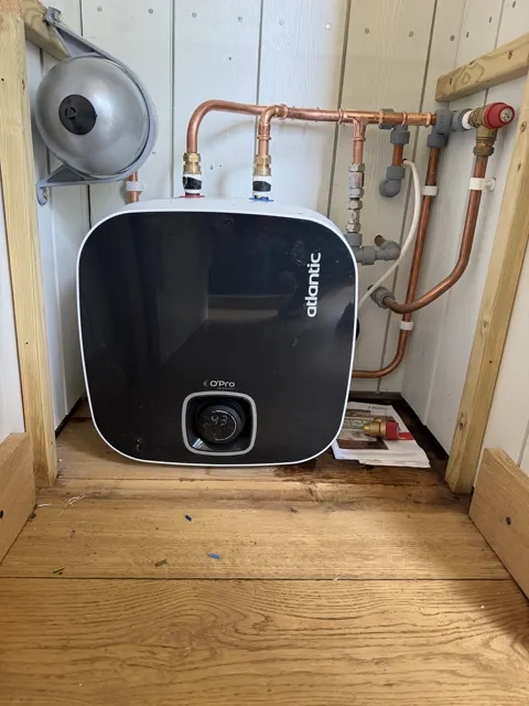 Black Atlantic water heater with copper pipework in a timber cupboard.