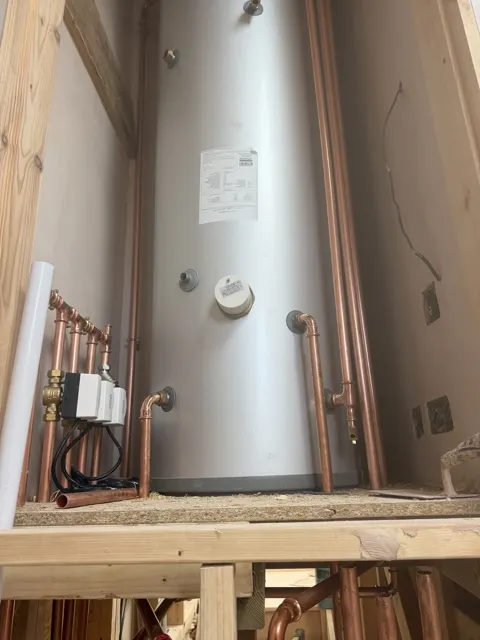 Tall unvented hot water cylinder with copper pipework in a timber-framed cupboard.