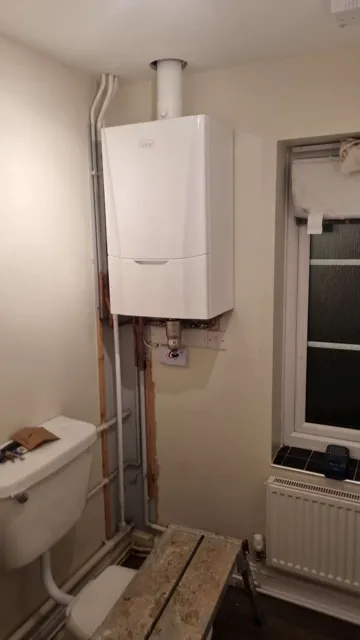Boiler and connected pipework beside kitchen units.