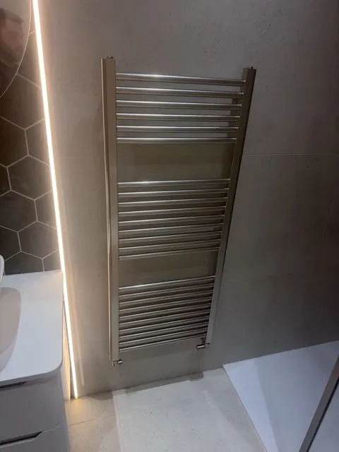 Chrome ladder towel radiator on a grey tiled bathroom wall.