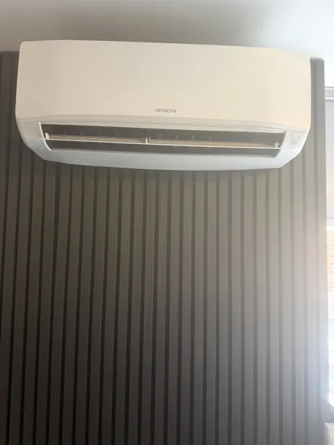 Hitachi indoor air-conditioning unit above dark panelling.